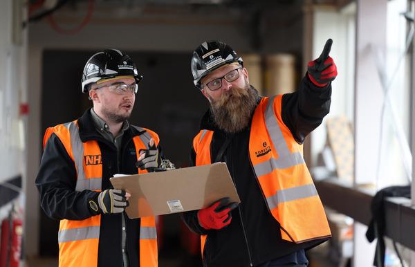 Two members of Team Robertson's construction team, both wearing PPE. One is holding a clipboard while the other points at part of the project.