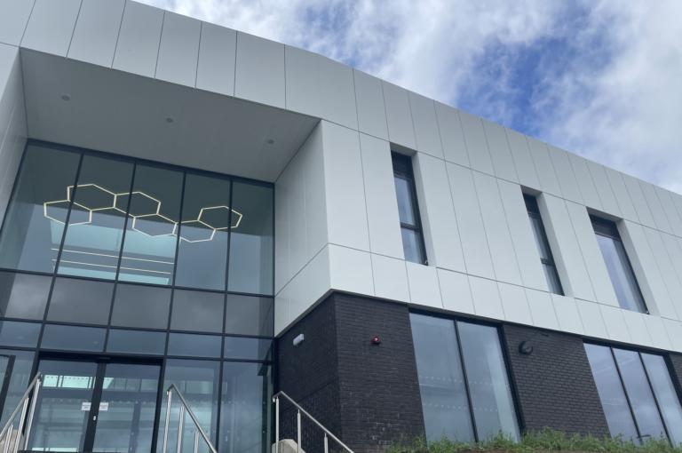 Image of outside of new college building upper half white lower half dark grey with glass entrance