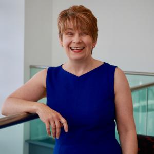 Katherine Macintosh, wearing a blue dress, smiling at the camera.