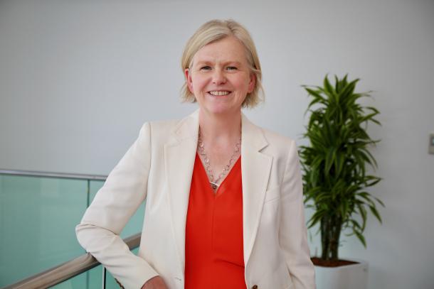 Charlotte Swanson, wearing a cream suit jacket and red blouse, smiling at the camera.