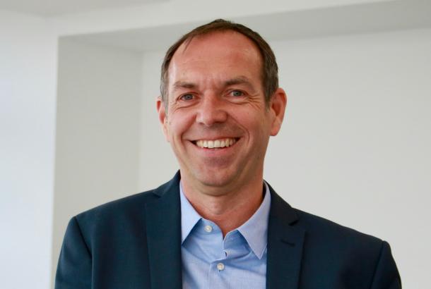 Colin Souter, wearing a dark suit and blue shirt, smiling at the camera.