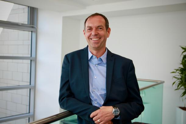 Colin Souter, wearing a dark suit and blue shirt, smiling at the camera.