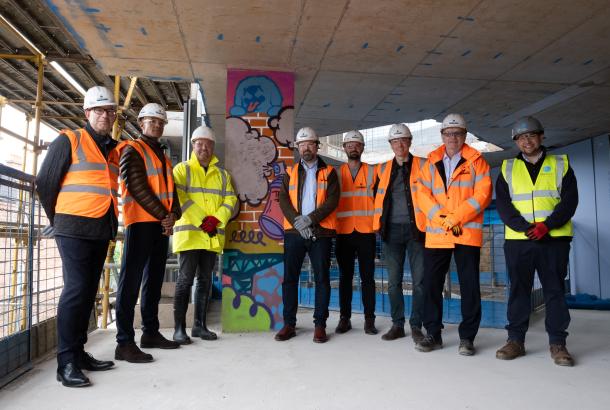 Eight people standing in PPE by a spray painted concrete pillar