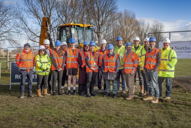 People in hi-vis at the groundbreaking of a new school project in Northumberland with a digger in the background on a field