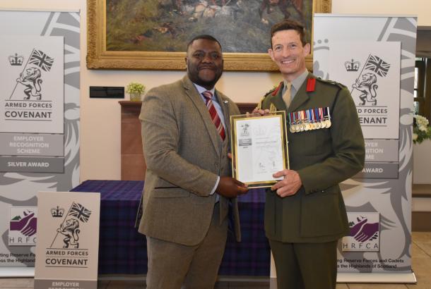 Robertson Group employee wearing a suit, collecting the Armed Forces Covenant Silver Award from a Brigadier with armed forces signage behind