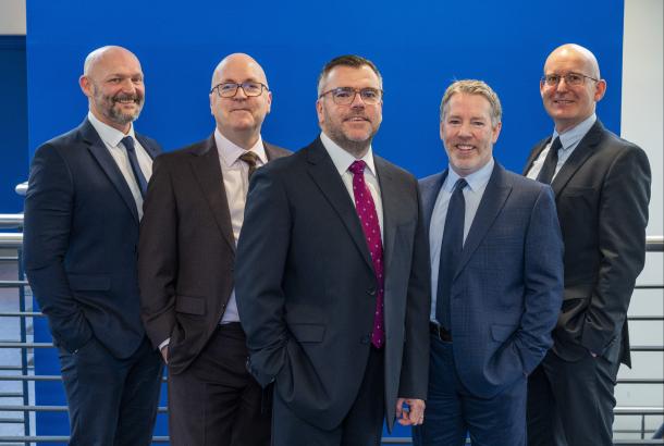 Five men in a mix of grey and navy suits stood together in front of a stairwell and blue wall, who are the new Robertson Partnership Homes Board 