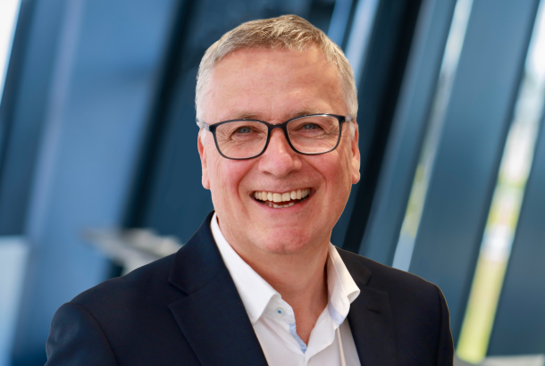headshot of a business executive in blue suit and white open necked shirt