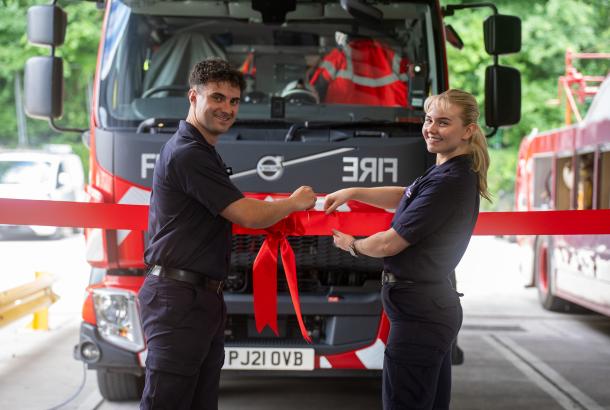 Blackley Community Fire Station official opening. Two firefighters cutting a red ribbon in front of a fire truck.