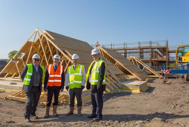 Image of men on construction site in front of timber frame construction in progress