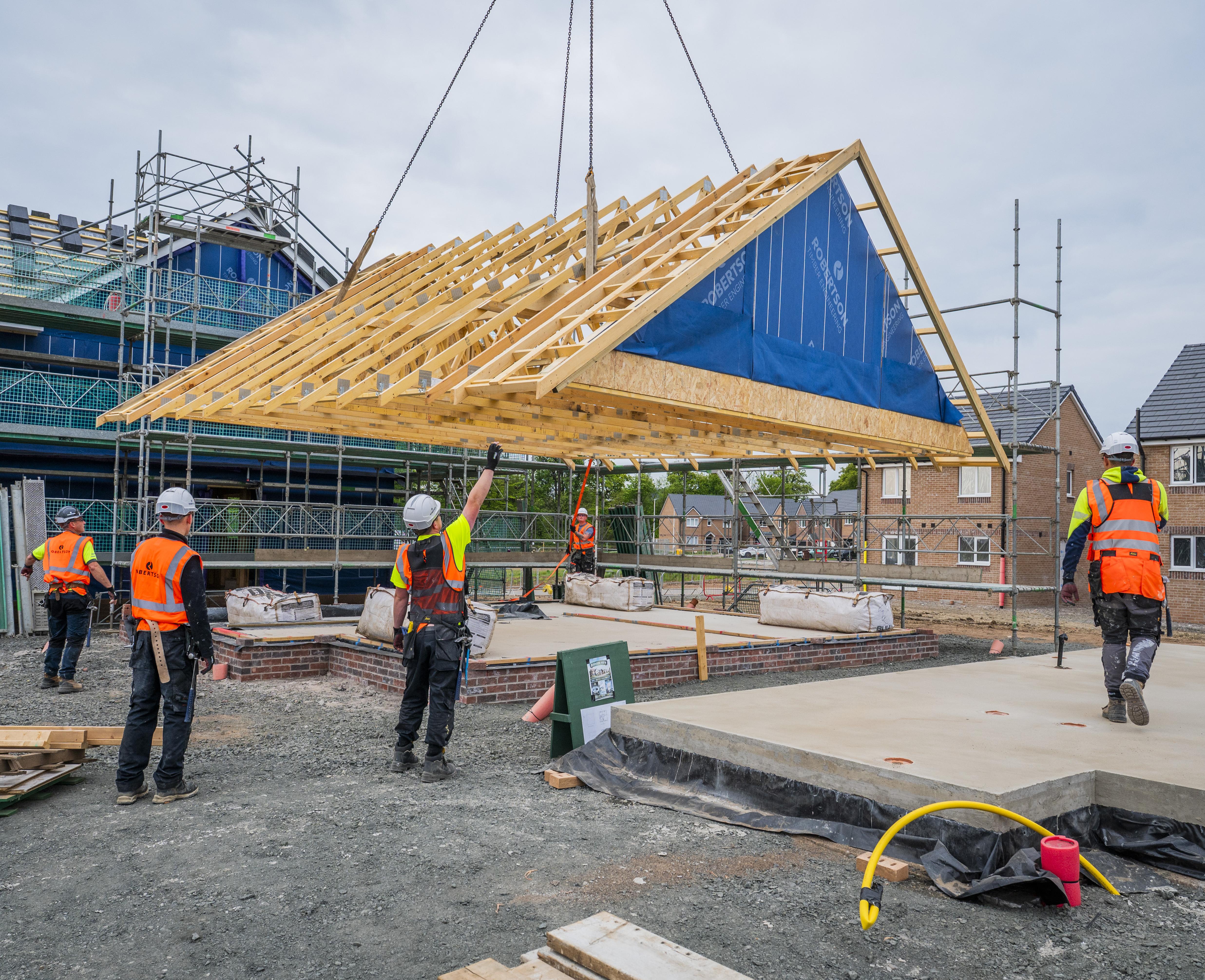 Timber roof frame being craned into place with men in hi viz overseeing