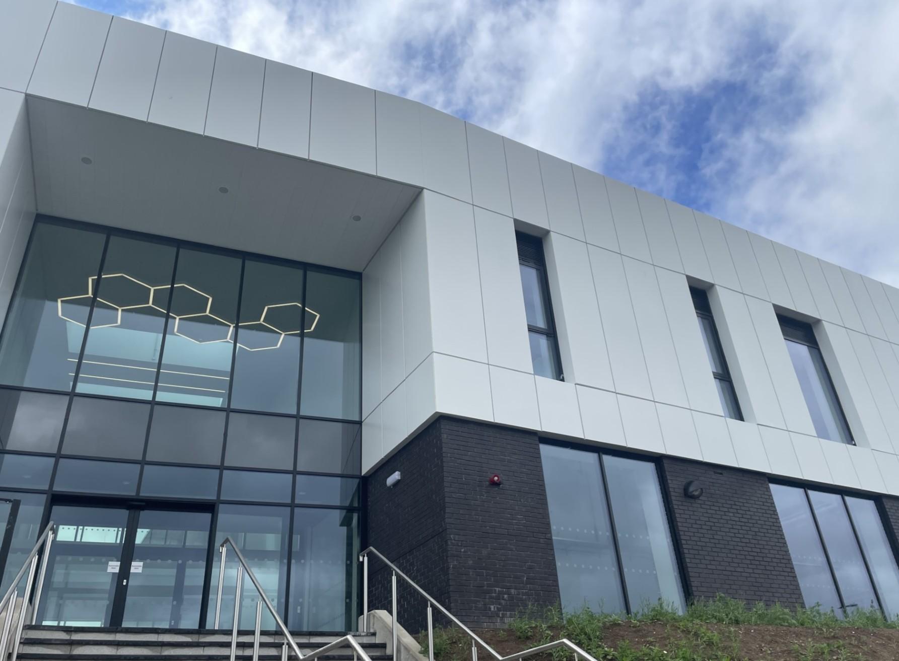 Image of outside of new college building upper half white lower half dark grey with glass entrance