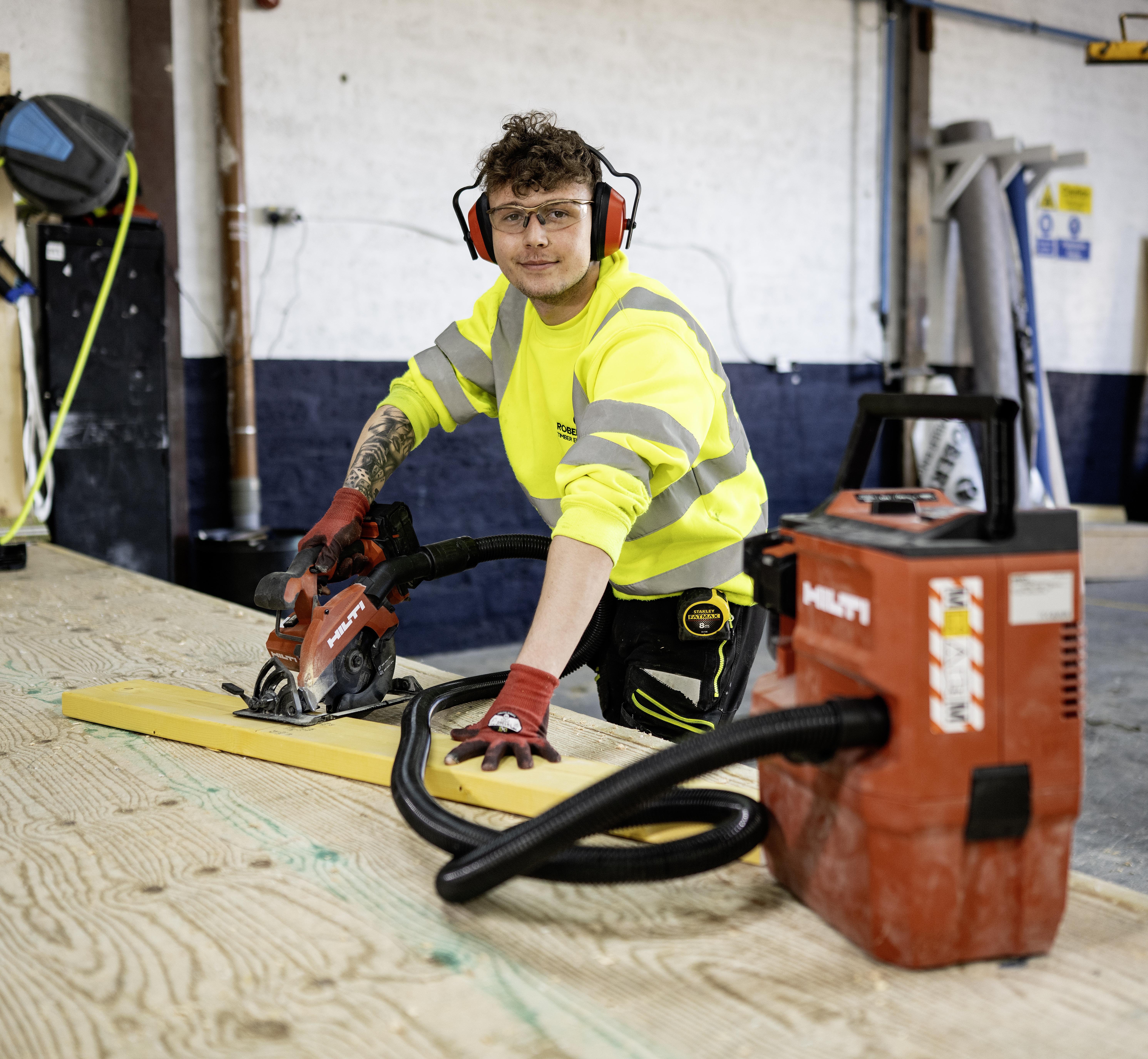 Image of timber factory worker with ear protection, gloves and dust extractor