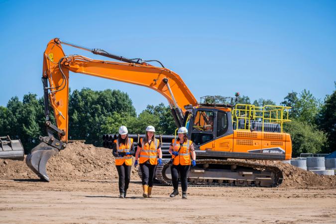 Three women in front of excavator