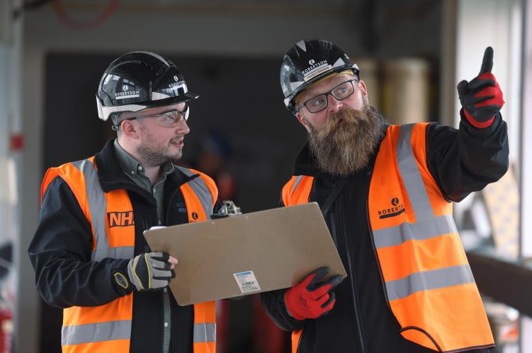 Two construction team members looking at a drawing and pointing.