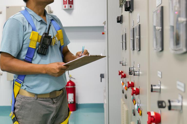 A man wearing a blue shirt and yellow harness is writing on a clipboard