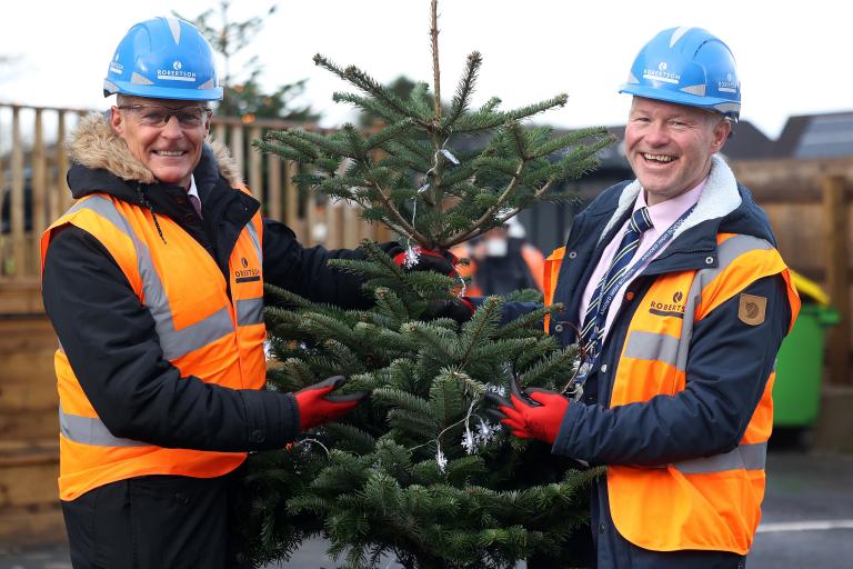 Head Teachers from Argoed High School and Ysgol Mynydd Isa Primary School hold a fir tree that Robertson gifted as part of Mynydd Isa's topping out