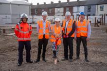 Robertson Construction employees with Greater Manchester Combined Authority and GMFRS for the groundbreaking of Whitefield community fire station, wearing PPE and Deputy Mayor holding a spade on the construction site