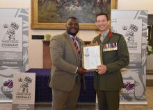 Robertson Group employee wearing a suit, collecting the Armed Forces Covenant Silver Award from a Brigadier with armed forces signage behind