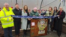 Row of people cutting a ribbon with wooden lectern in centre