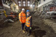 Two people in PPE, one from Robertson Construction and the other from Royal High School Preservation Trust, standing in the grand hall of the National Centre for Music to announce the project commencing.