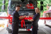 Blackley Community Fire Station official opening. Two firefighters cutting a red ribbon in front of a fire truck.