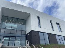 Image of outside of new college building upper half white lower half dark grey with glass entrance