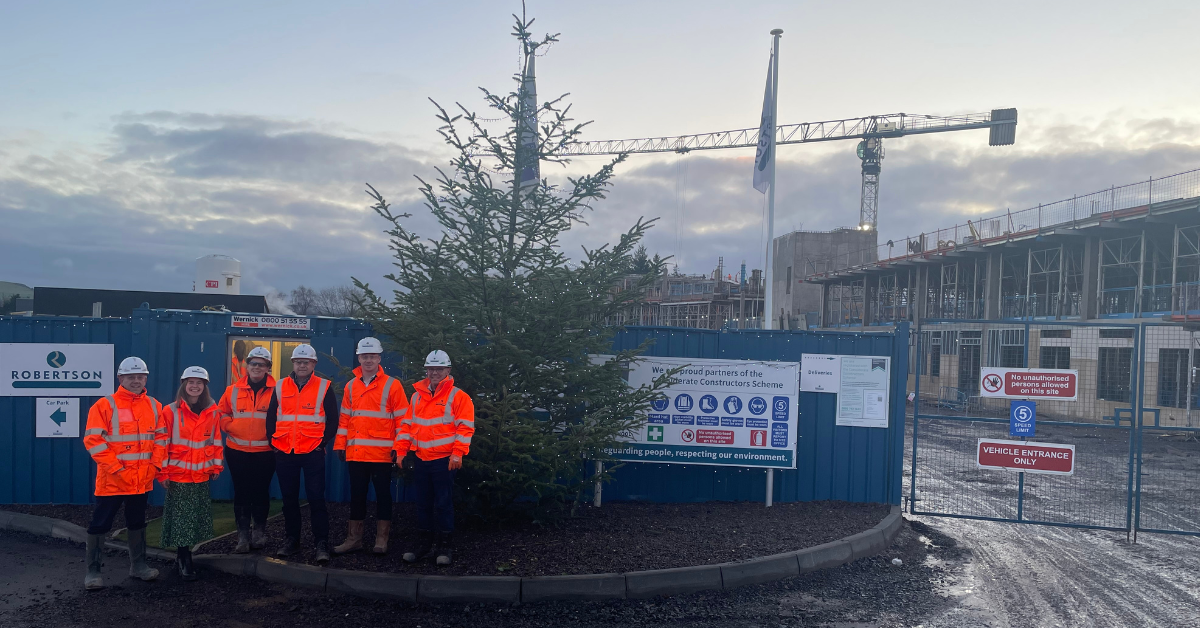 Robertson Construction Tayside site team at Perth High School standing in front of a Christmas tree and Perth High School where a new school is being constructed
