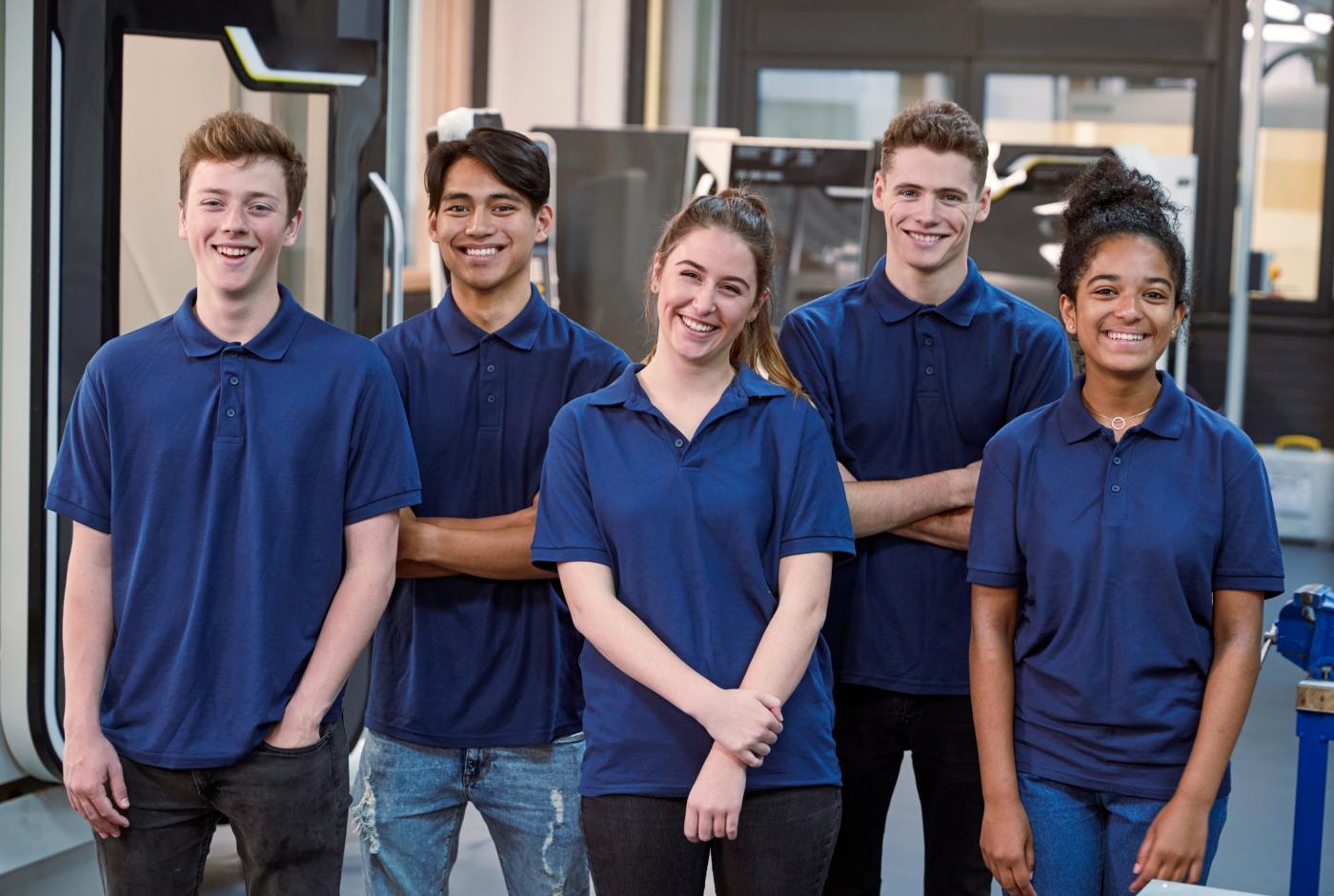 Five young people wearing blue t-shirts, in a line, smiling at the camera.
