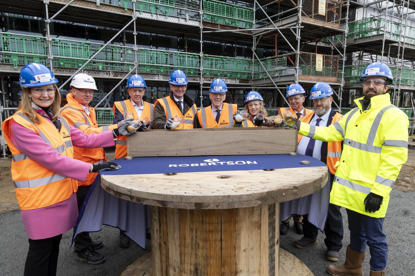 People surrounding a table at a construction site pouring ingredients into a brick mould