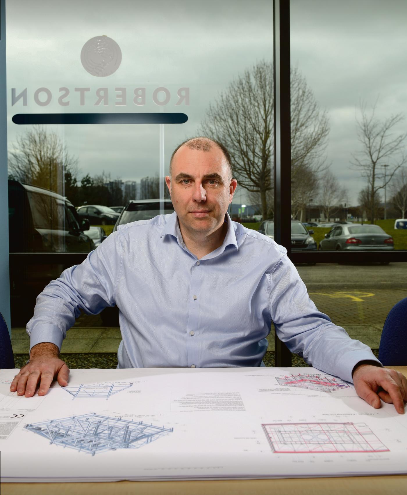 Man sat by a table with blueprints of a project