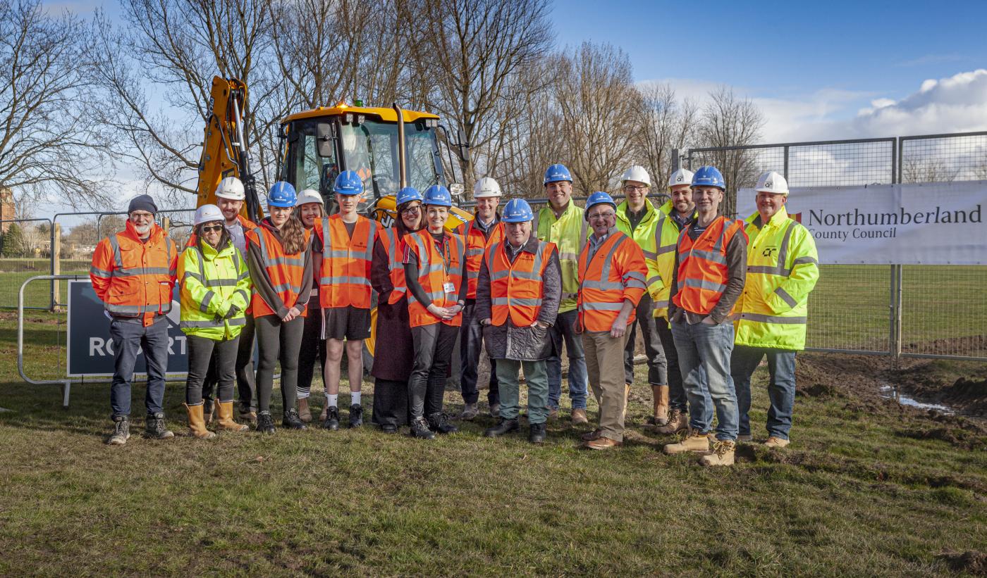 People in hi-vis at the groundbreaking of a new school project in Northumberland with a digger in the background on a field