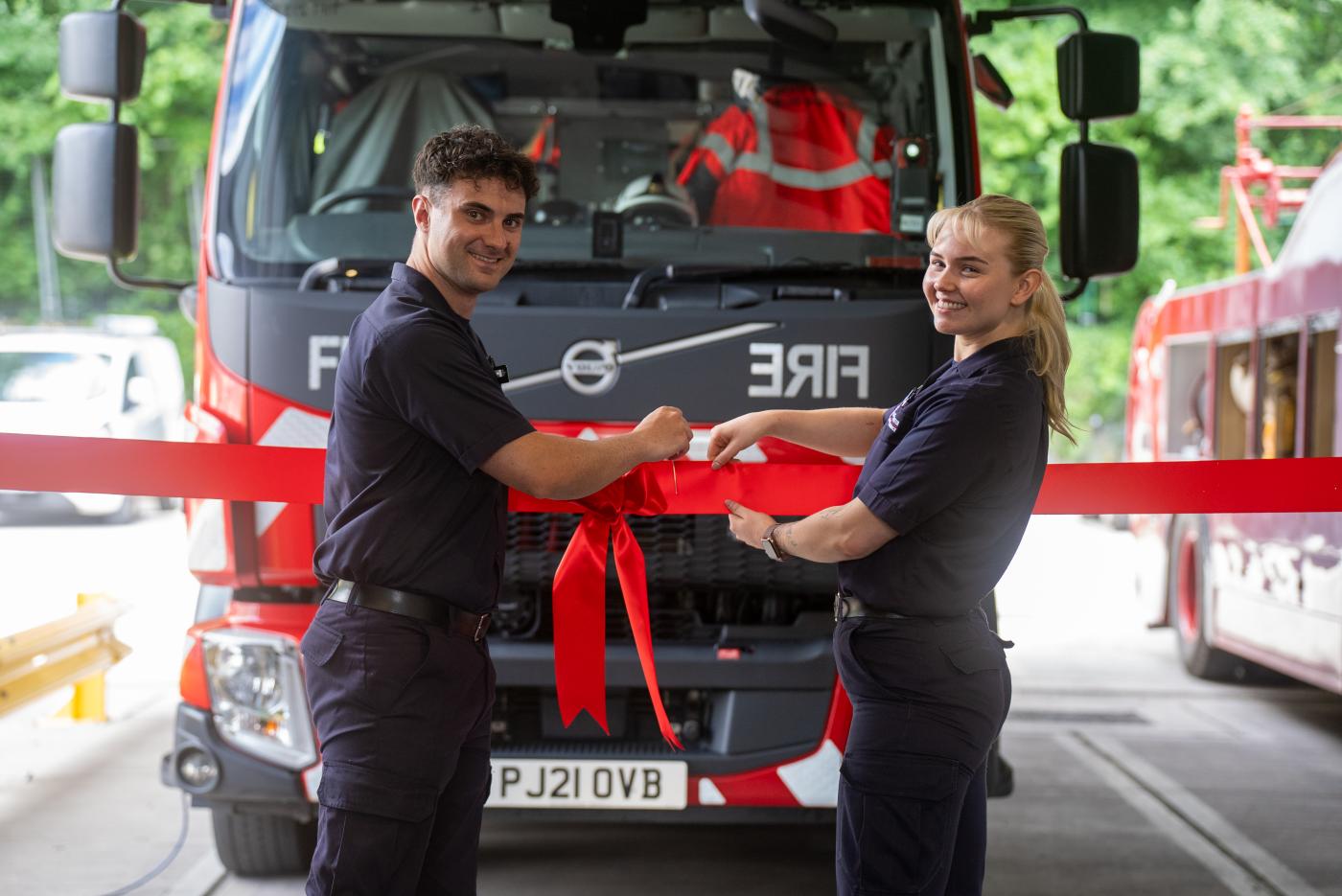 Blackley Community Fire Station official opening. Two firefighters cutting a red ribbon in front of a fire truck.
