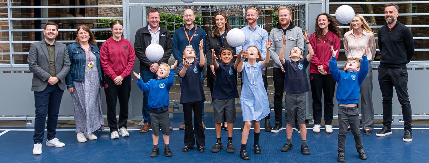 Group of pupils throwing footballs in the air with adults standing behind