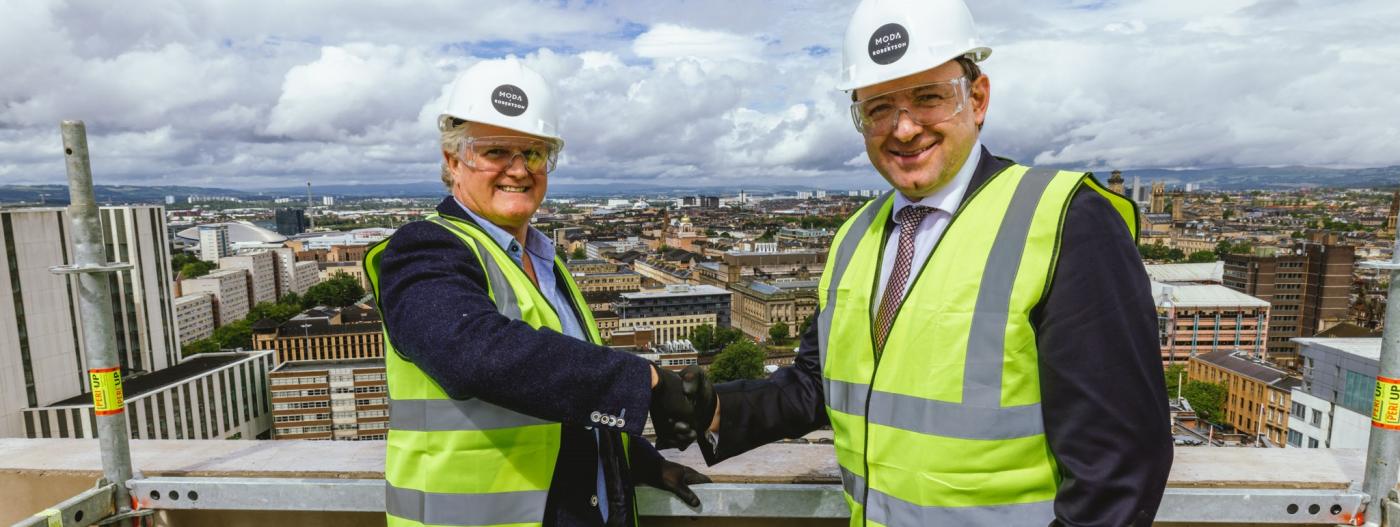 Tony Brooks, Managing Director at Moda Living and Elliot Robertson, Chief Executive, Robertson Group, both dressed in PPE, shaking hands.